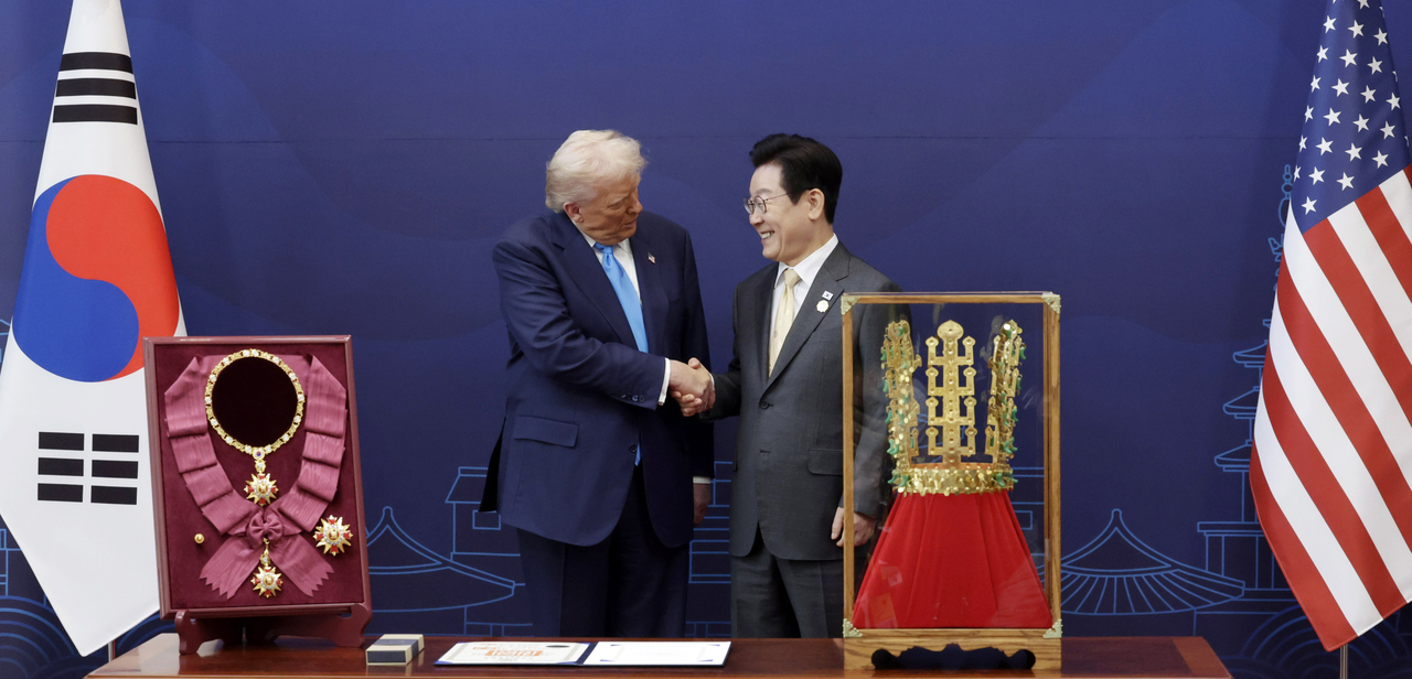 South Korean President Lee Jae Myung (right) shakes hands with US President Donald Trump after presenting Trump the Grand Order of Mugunghwa (left), Korea's highest honor reserved for heads of state and a replica of the Gold Crown from Cheonmachong, one of Korea's surviving ancient crowns, during the two states' bilateral talks on the sidelines of the APEC summit on Wednesday. (Pool photo via Yonhap)