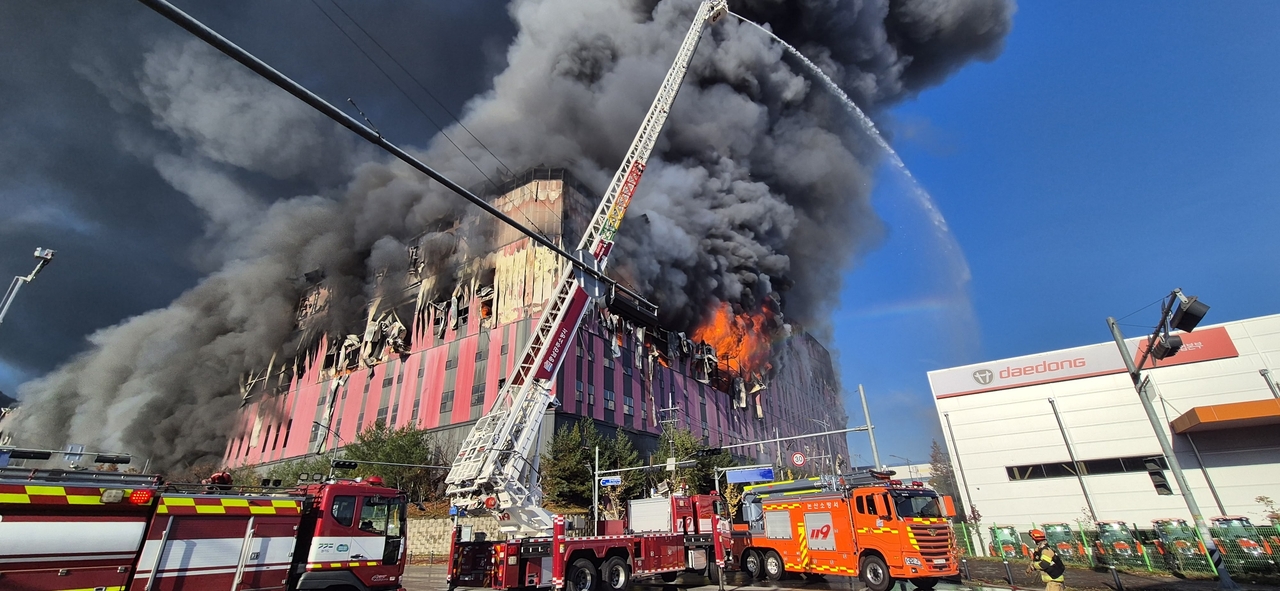 Flames tear through the upper floors of the E-Land warehouse in Cheonan, South Chungcheong Province, on Saturday as firefighters battle intense heat and collapsing walls. (Yonhap)